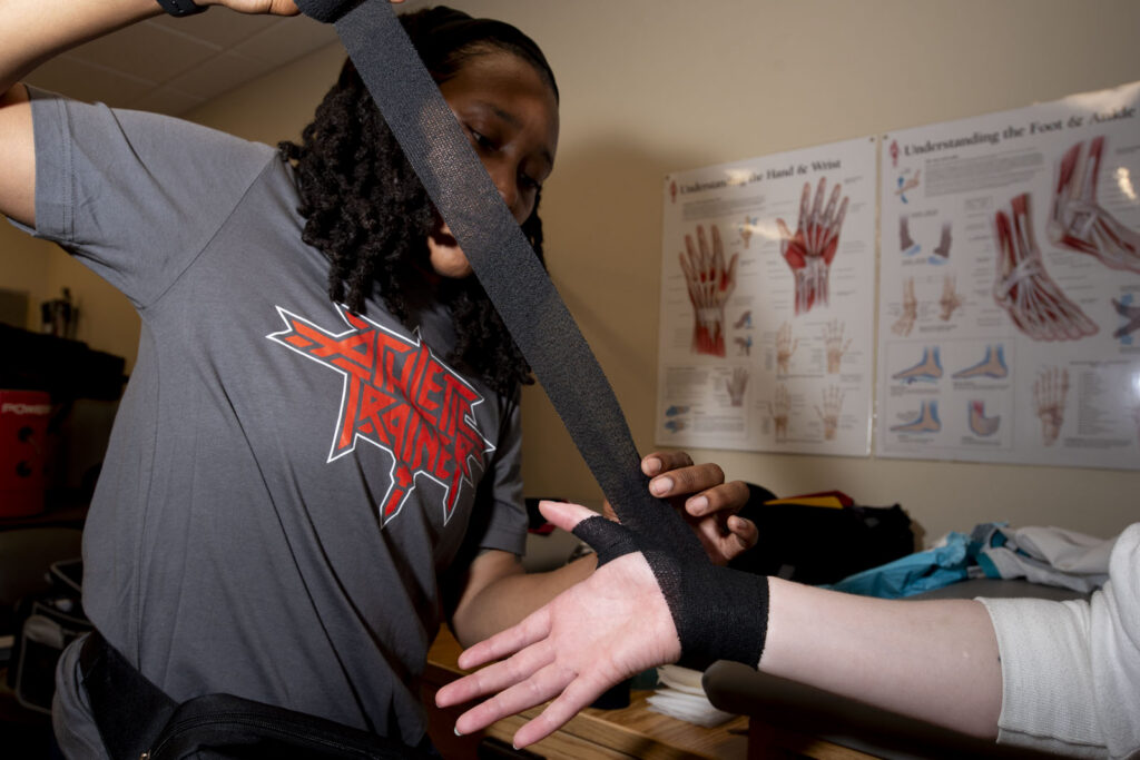 Athletic Trainer Asia McCants wraps a football player's wrist in pre-wrap before a football game.