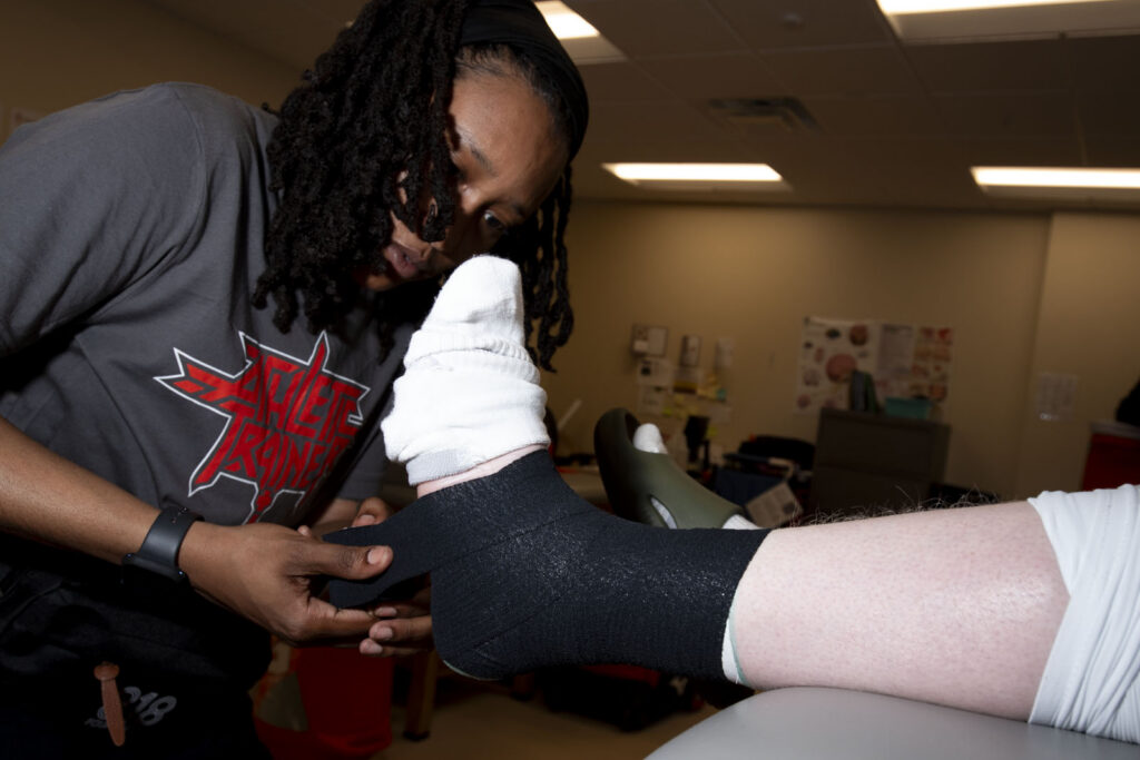 Athletic Trainer Asia McCants wraps a football player's ankle before a football game.